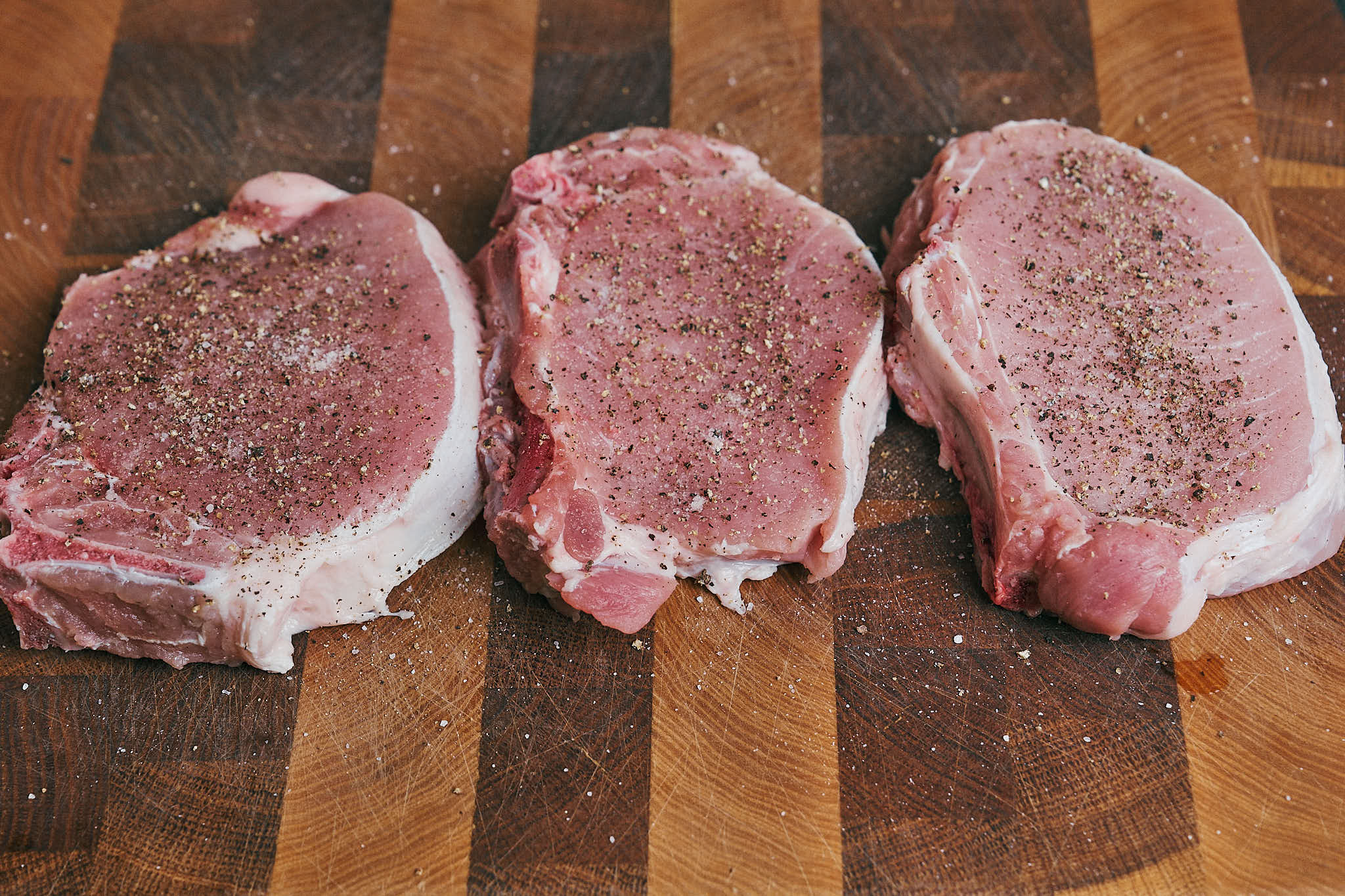 Three seasoned pork chops resting before searing