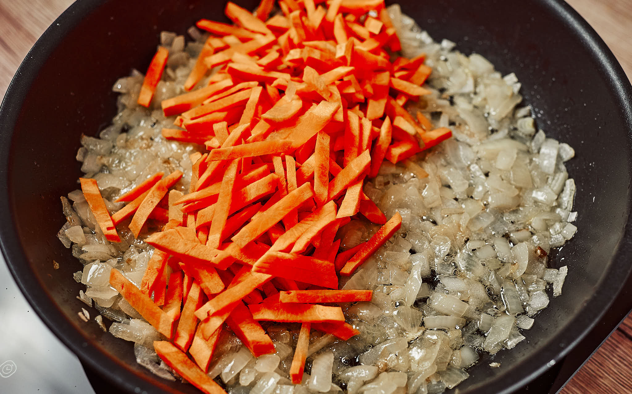 Grated carrot added to sautéed onion in a pan