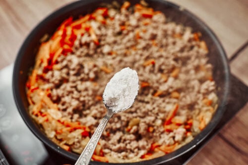 Salt being added to ground beef and vegetables in a pan