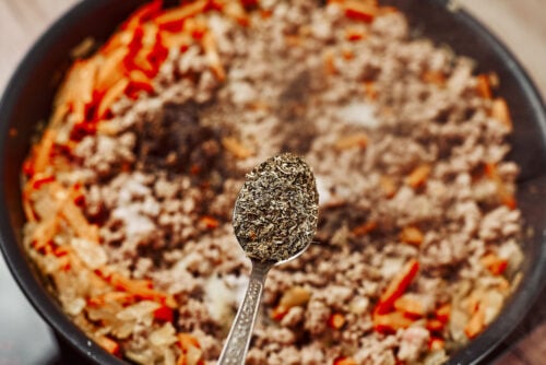 Dried herbs and spices added to ground beef in a skillet