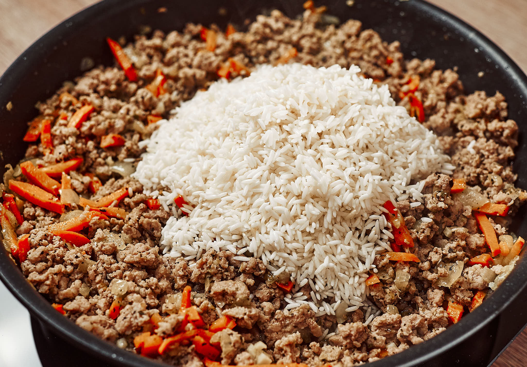 Rinsed white rice added to cooked ground beef and vegetables in a pan