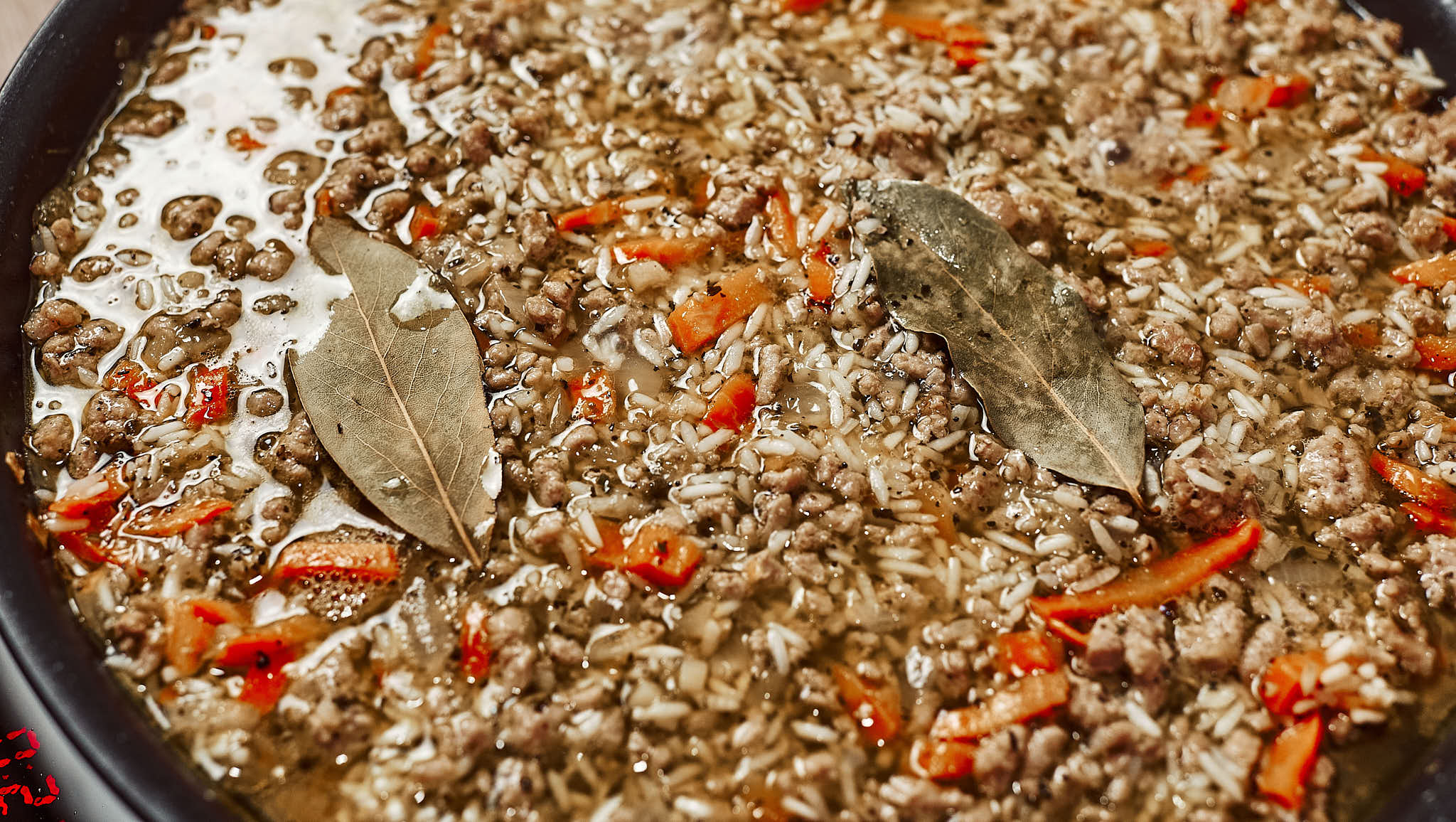 Water and bay leaves added to ground beef and rice in a skillet