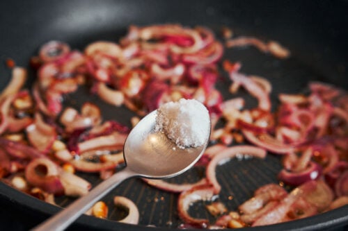 Salt sprinkled over onions as they soften in the skillet