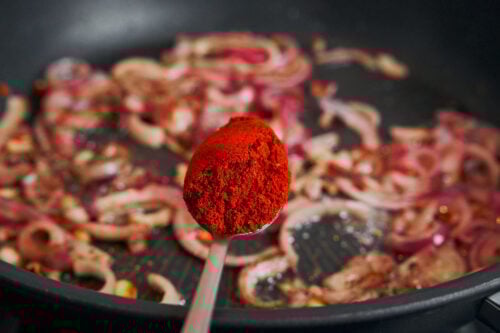 Smoked paprika being added to onions for deep flavor

