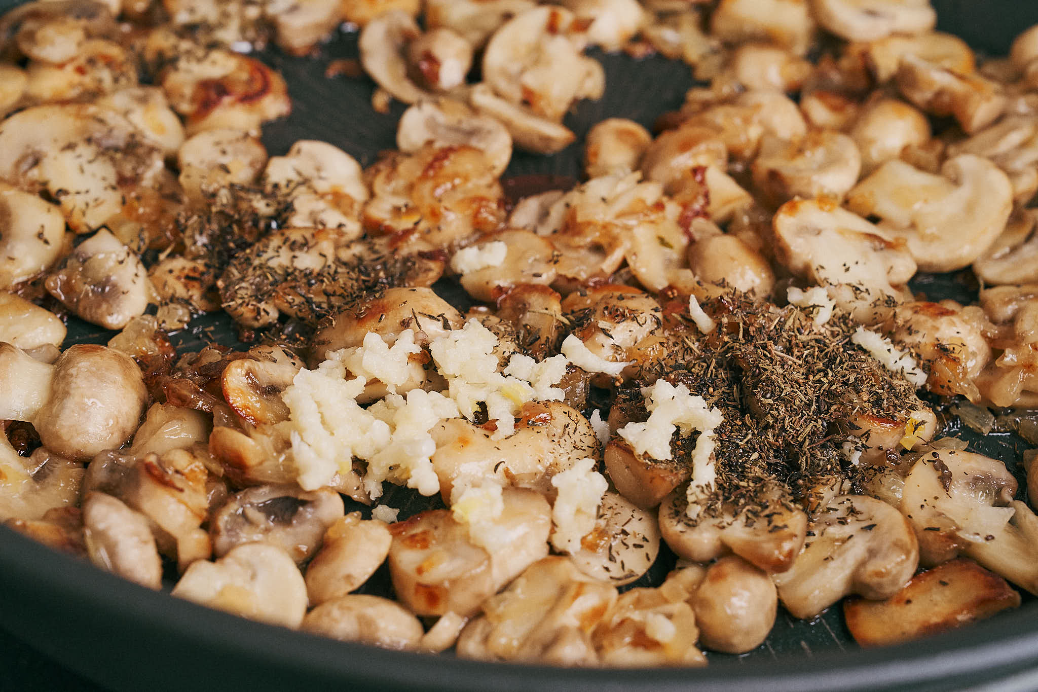 garlic and thyme added to sautéed mushrooms in the skillet