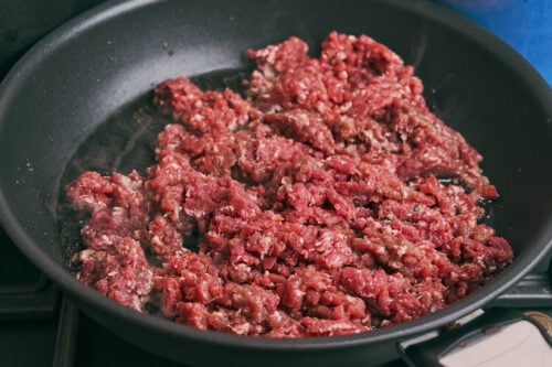 raw ground beef added to a skillet for browning