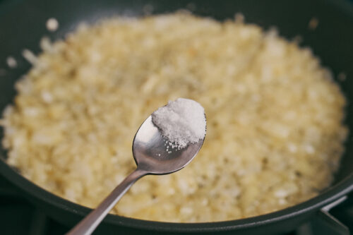 Adding salt to sautéed onions in a skillet

