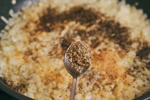 Adding oregano to onions for creamy ground beef pasta
