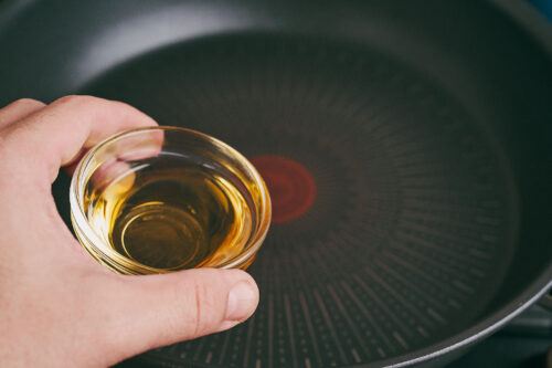 Olive oil being added to a skillet to start cooking ground beef