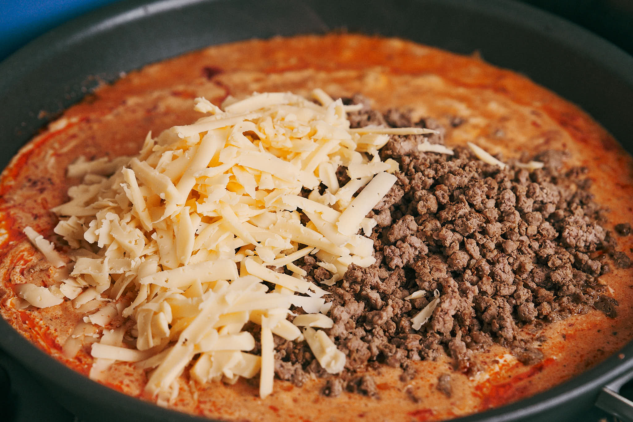 Adding ground beef and cheese to creamy ground beef pasta sauce
