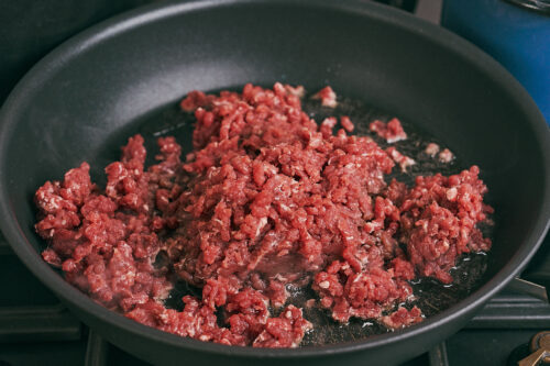 Raw ground beef added to a skillet for browning