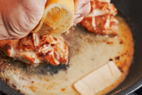 Lemon juice added to butter sauce while chicken cooks in a skillet