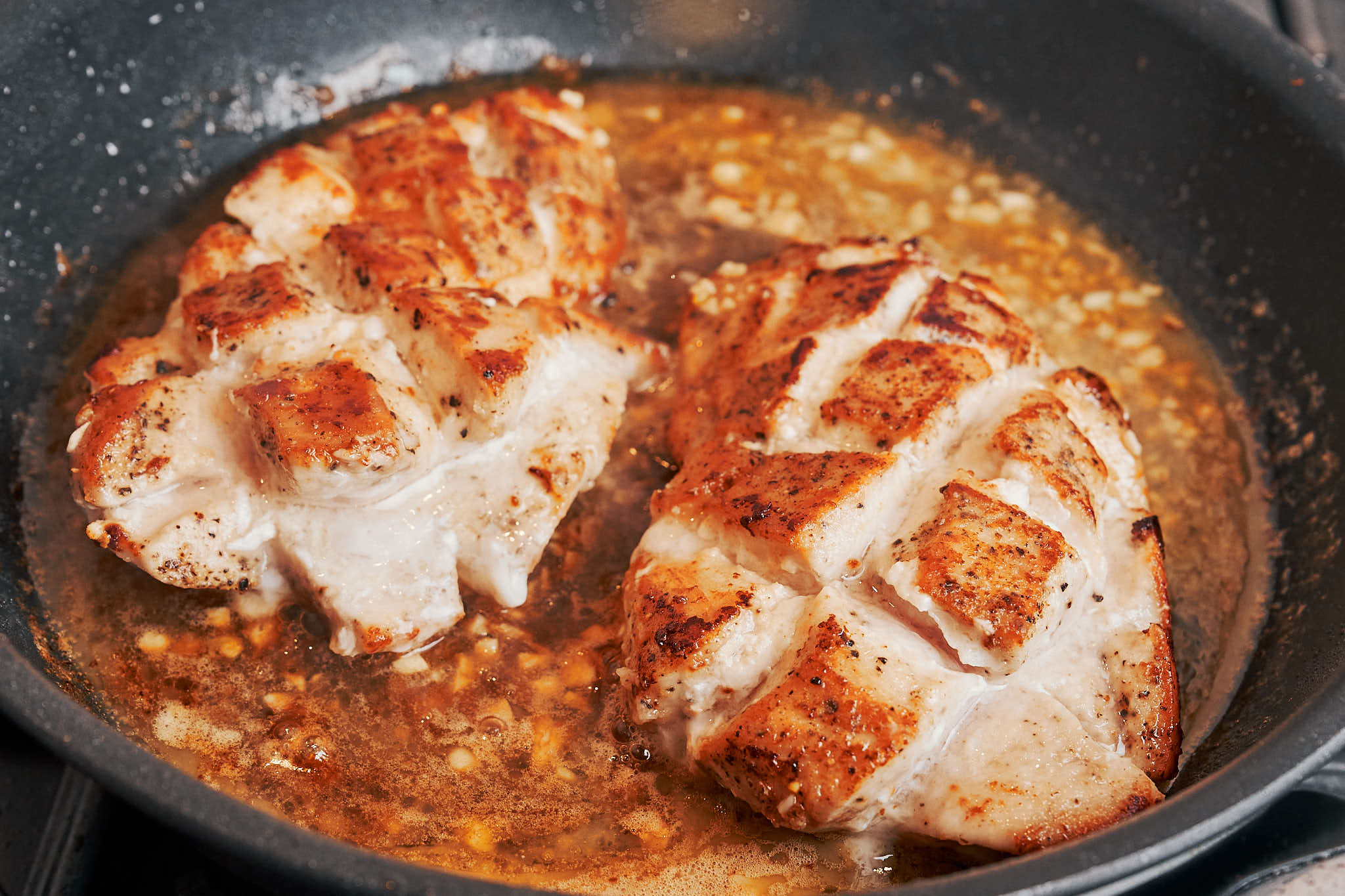 Chicken gently simmering in lemon honey butter sauce in a skillet