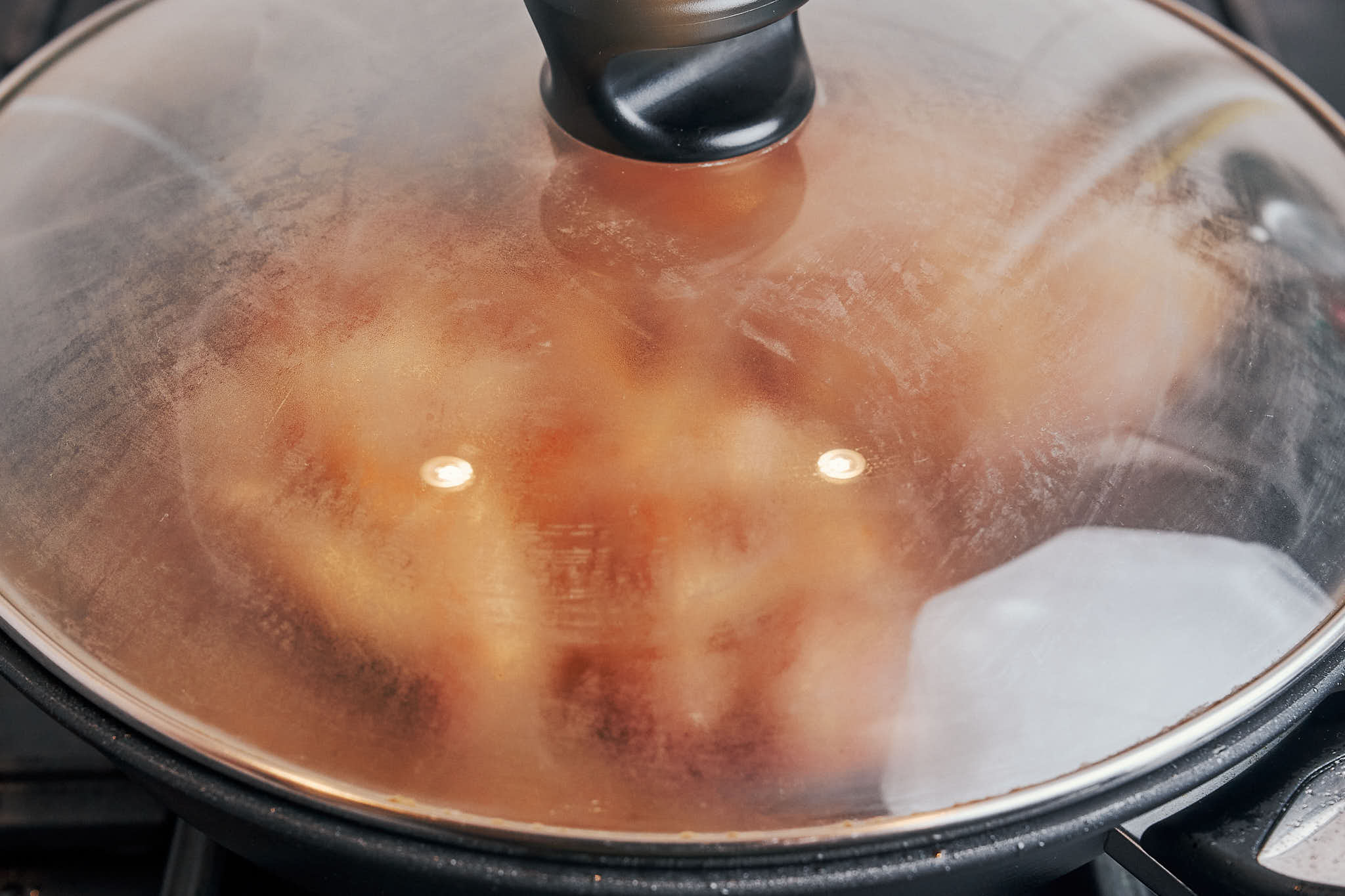 Chicken simmering under a lid in a skillet over low heat