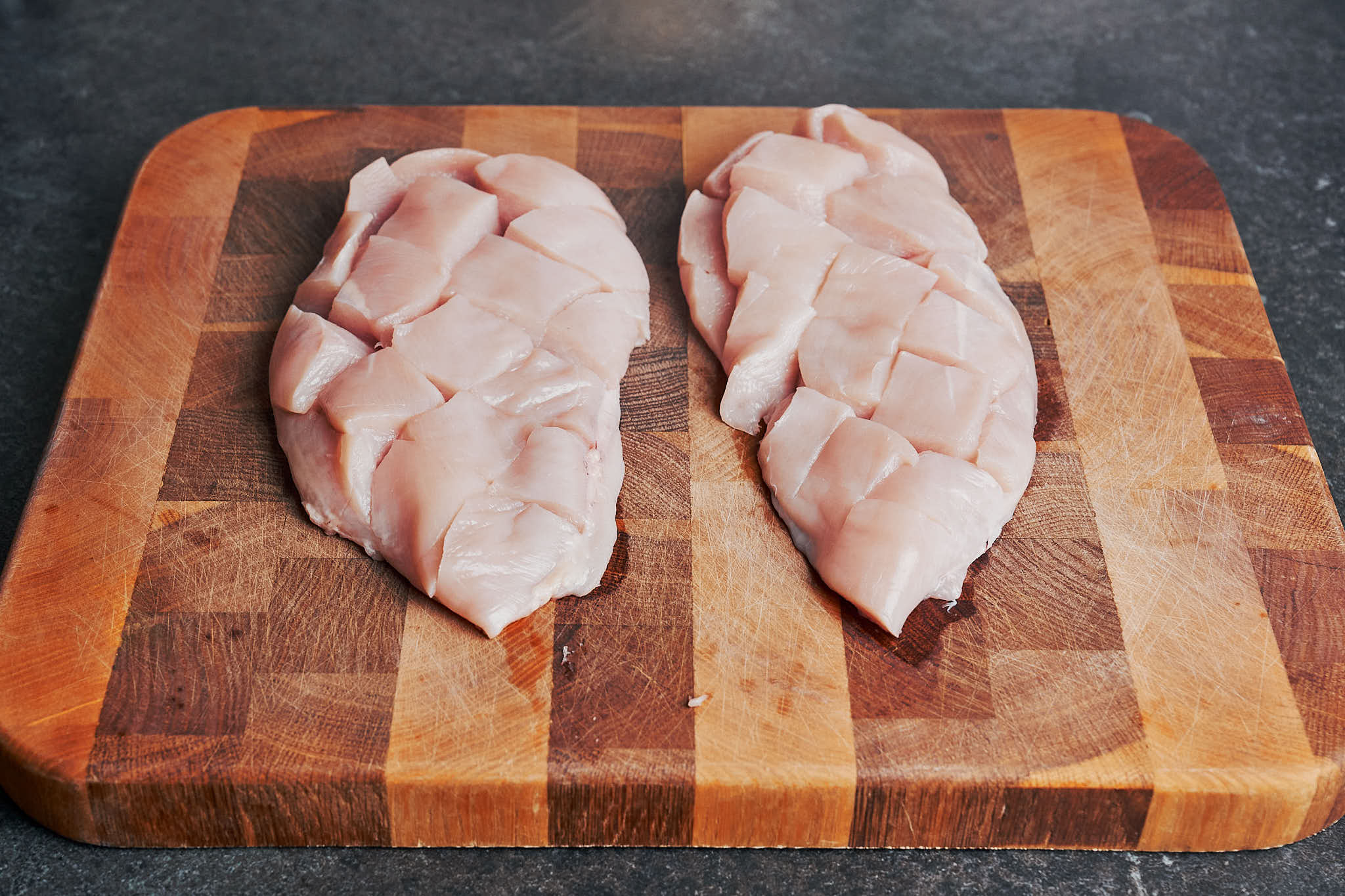 Chicken with crosshatch cuts on a wooden cutting board