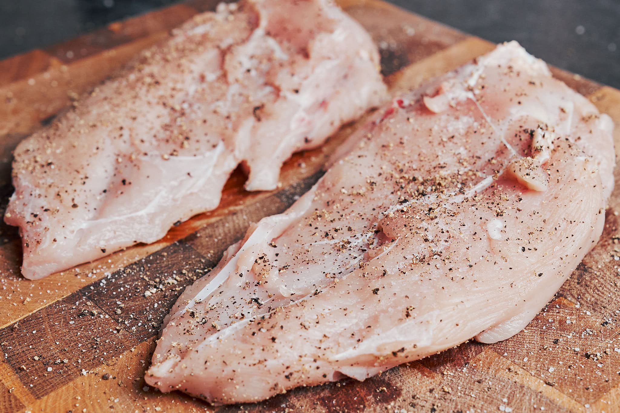 Seasoned chicken prepared for pan searing on a wooden cutting board