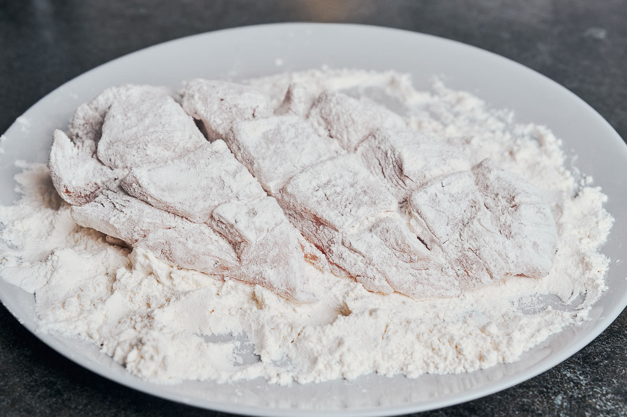 Chicken lightly coated with flour on a plate before pan searing