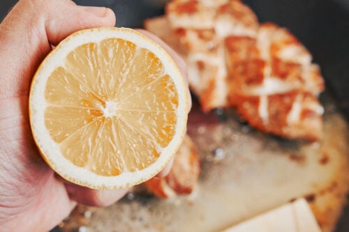 Fresh lemon half being squeezed over chicken in a skillet
