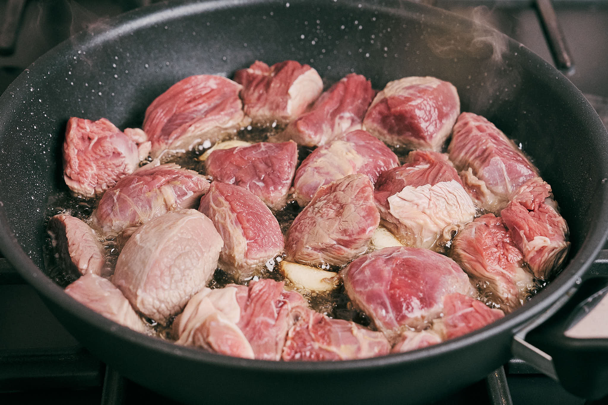 Raw beef pieces searing in hot oil in skillet