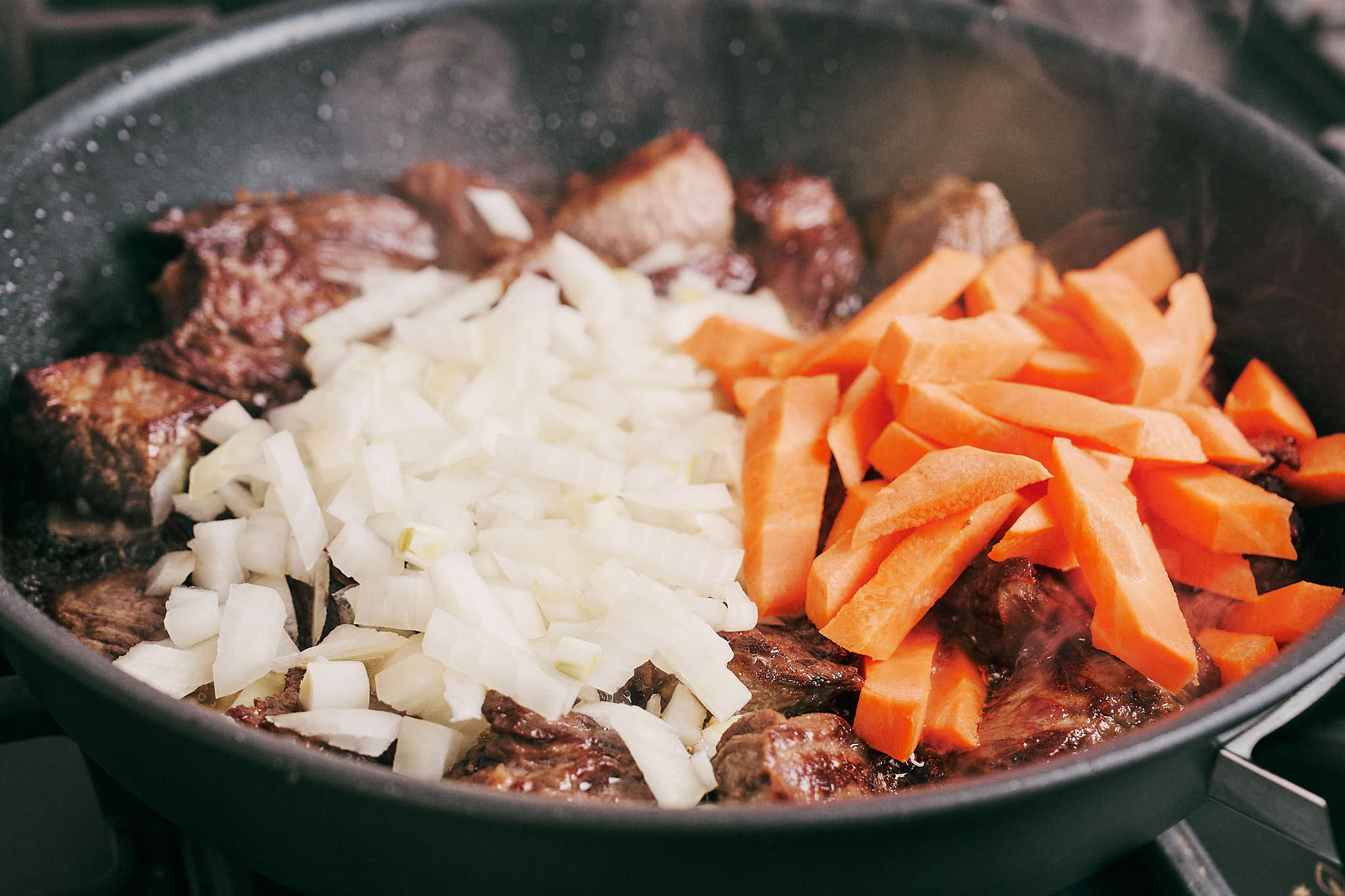 Onion and carrot added to beef in skillet