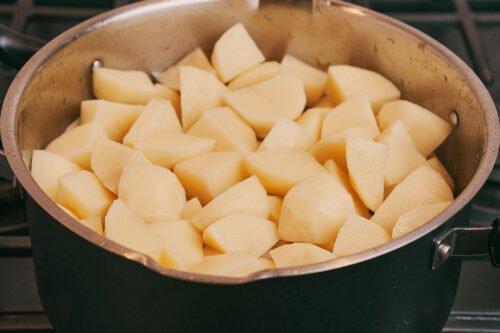 Cubed potatoes layered over pork and vegetables in a pot