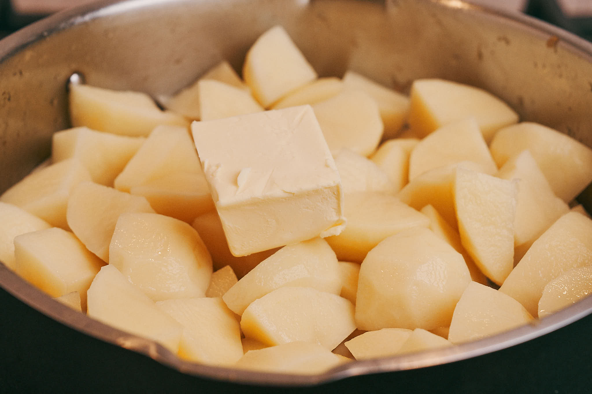 Cubed potatoes topped with butter in a pot before simmering