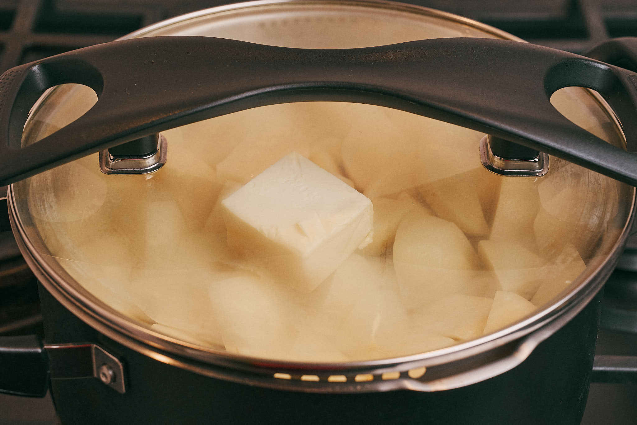 Potatoes and pork simmering covered with a lid on the stove