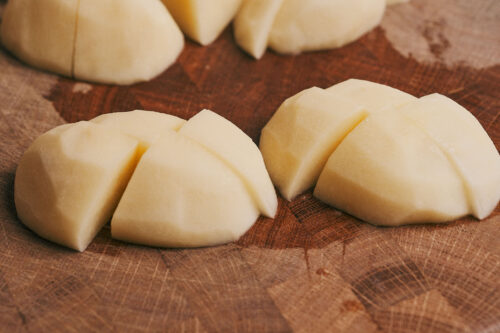 Potatoes cut into large chunks on a cutting board