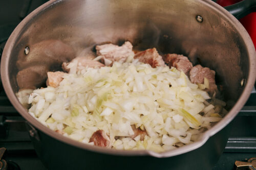 Chopped onion added to browned pork in a pot