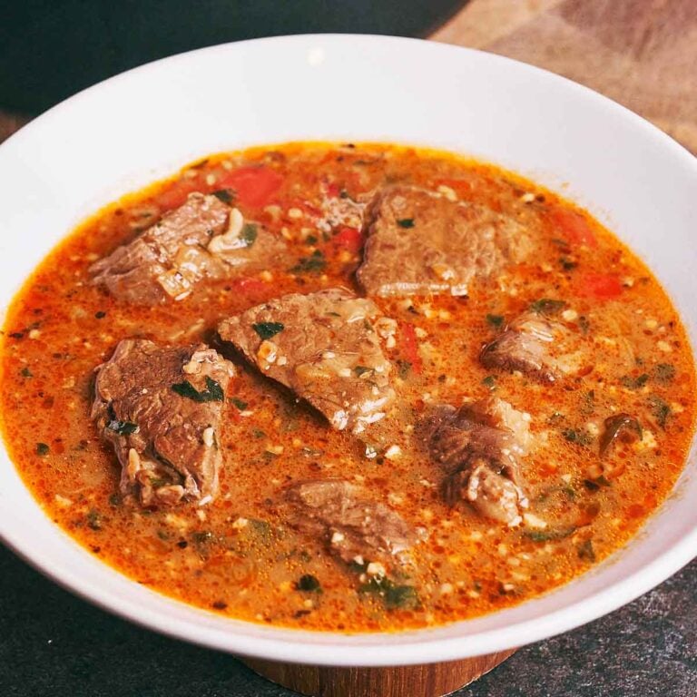 Hearty beef soup with walnuts, rice, and pomegranate broth served in a white bowl