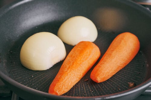 Whole onion and carrot roasting in a dry pan for beef soup broth