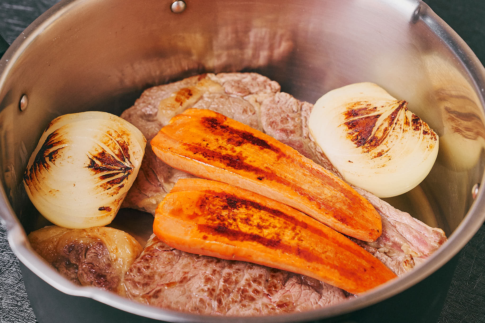 Beef on the bone with roasted onion and carrot in a pot before making broth
