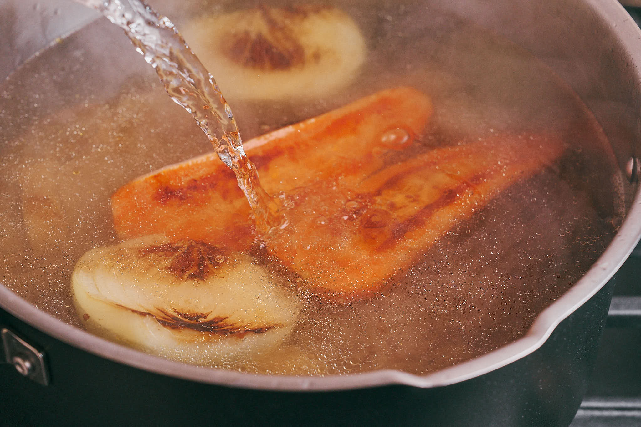 Pouring water over beef, onion, and carrot to start simmering the soup