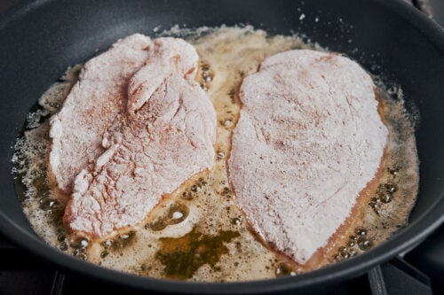 Floured chicken breasts added to a skillet for searing