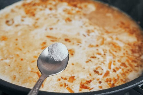 Salt being added to the creamy sauce in the skillet"