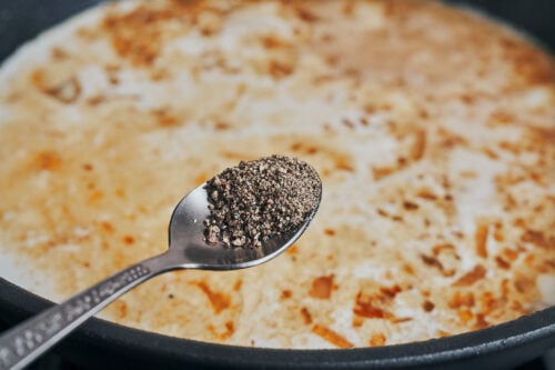 Black pepper being added to the creamy garlic sauce