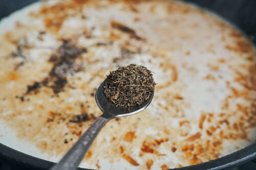 Thyme being added to the creamy garlic sauce
