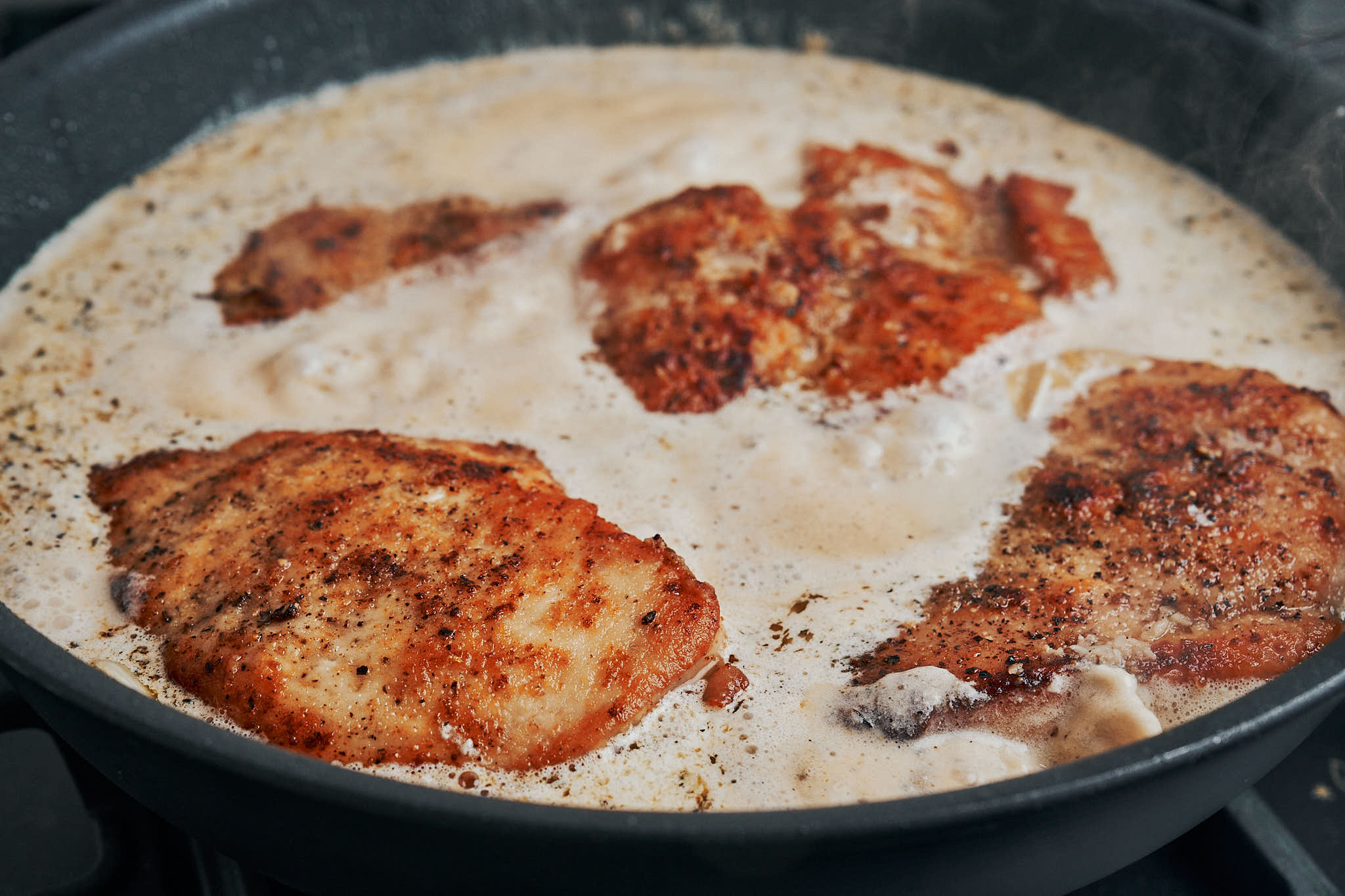Chicken breasts simmering in creamy garlic sauce in a skillet
