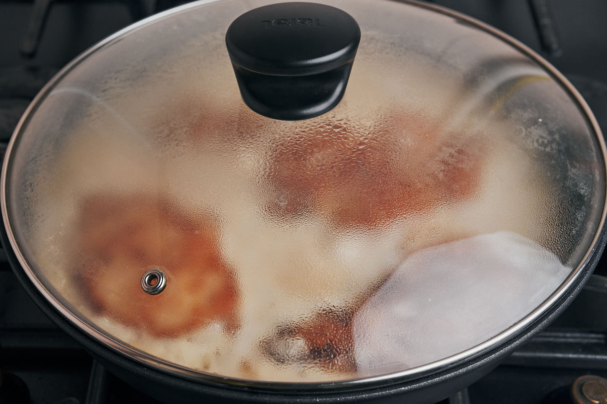 Chicken breasts simmering in creamy garlic sauce covered with a lid