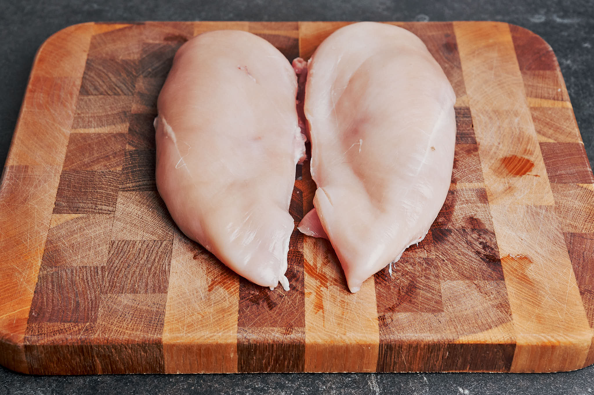 Raw chicken breasts on a cutting board before slicing