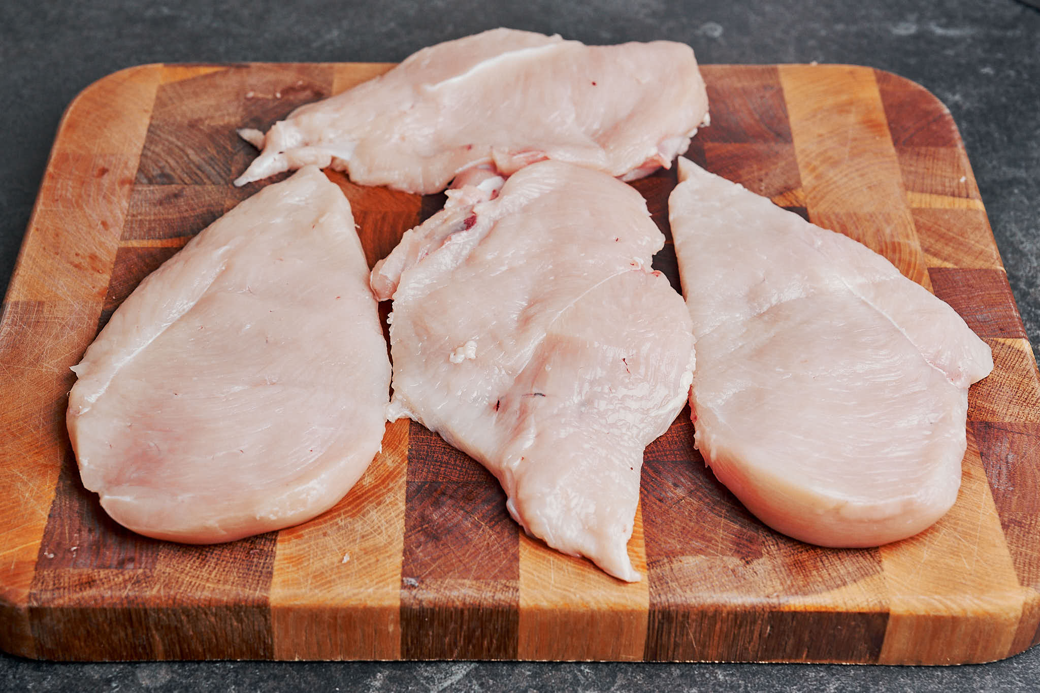 Chicken breasts sliced in half horizontally on a cutting board