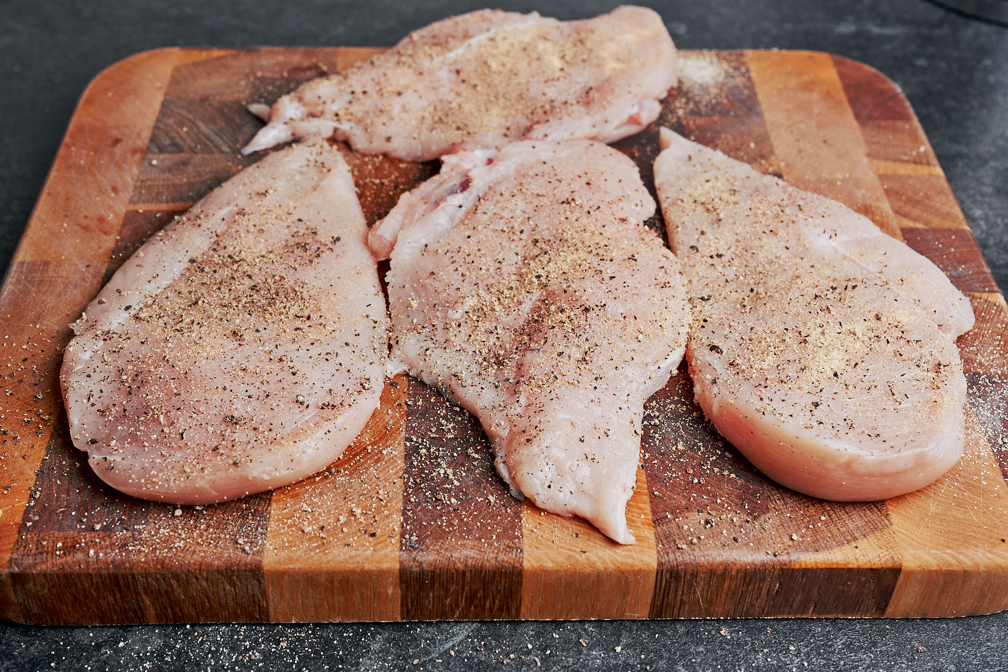 Seasoned chicken breasts with salt, pepper, and garlic powder on a cutting board