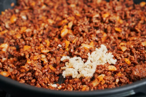 Ground beef cooking with minced garlic in a skillet