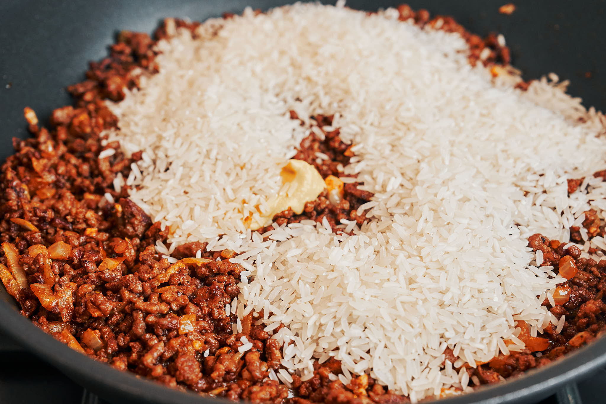 Long-grain white rice added to seasoned ground beef in a skillet