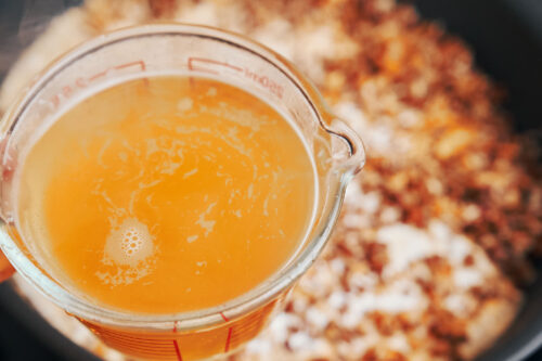 Adding beef broth to ground beef and rice in a skillet
