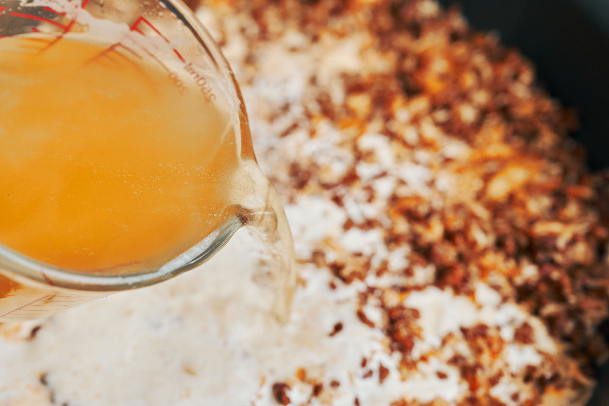 Pouring beef broth into ground beef and rice mixture