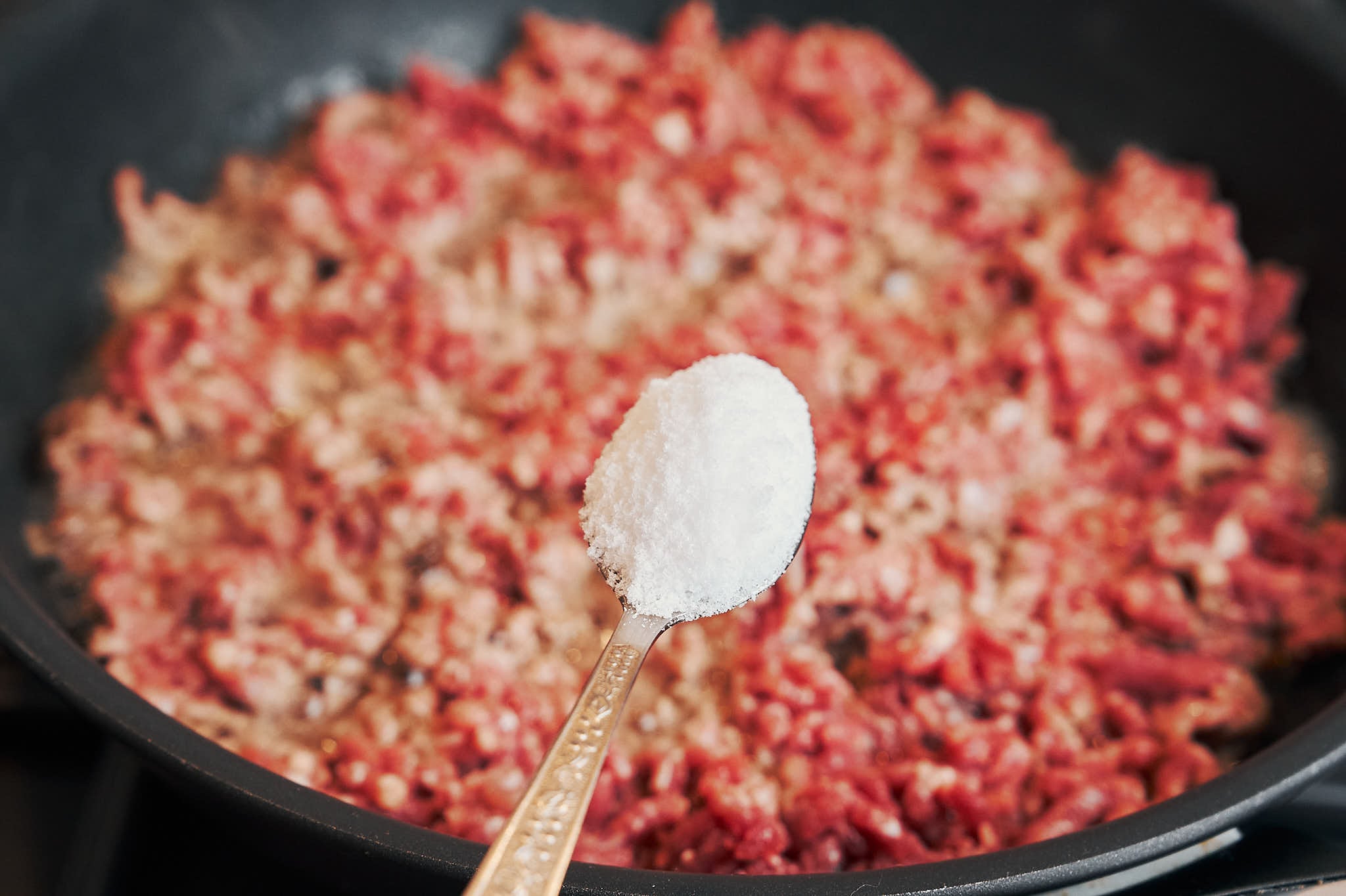 Seasoning ground beef with salt in a skillet