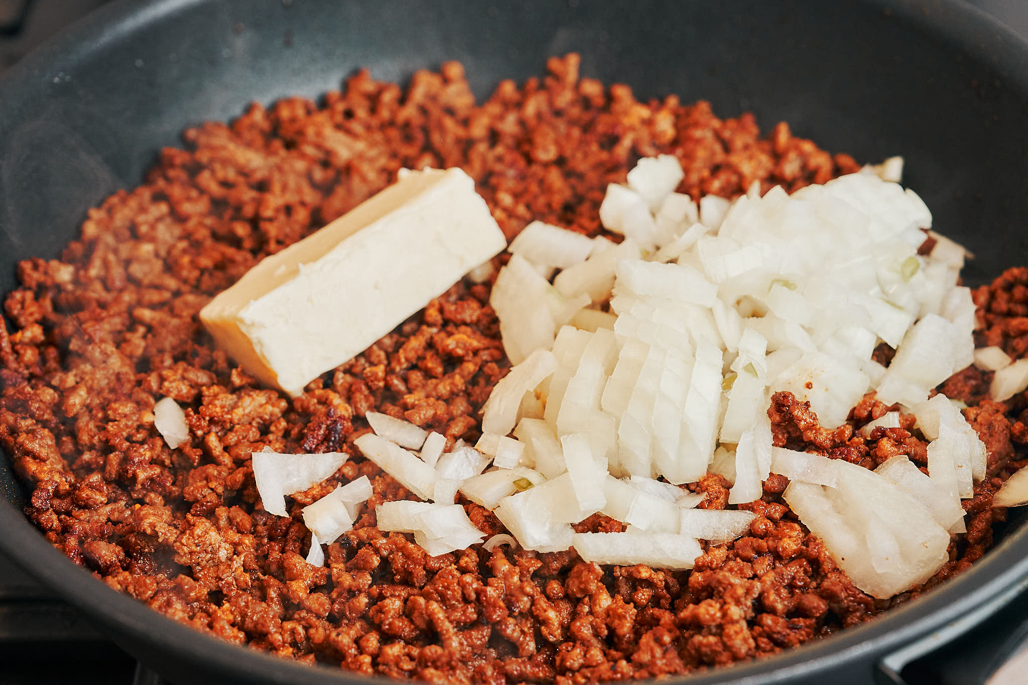 Adding butter and diced onion to browned ground beef in a skillet
