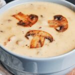 Creamy mushroom soup topped with sautéed mushroom slices in a blue bowl