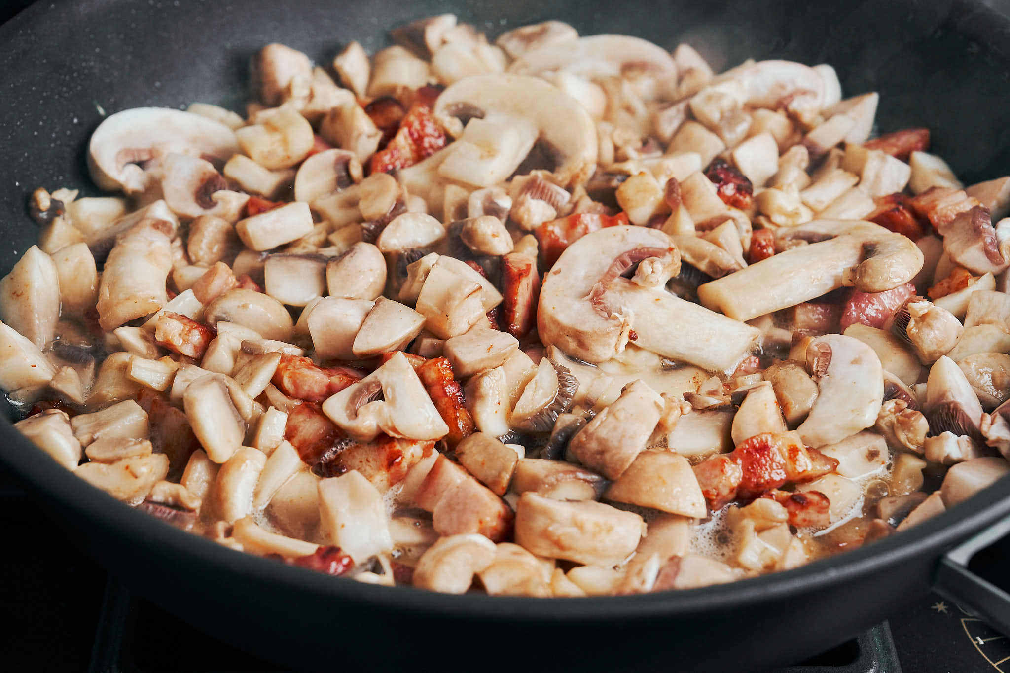 mushrooms sautéing with bacon in a skillet